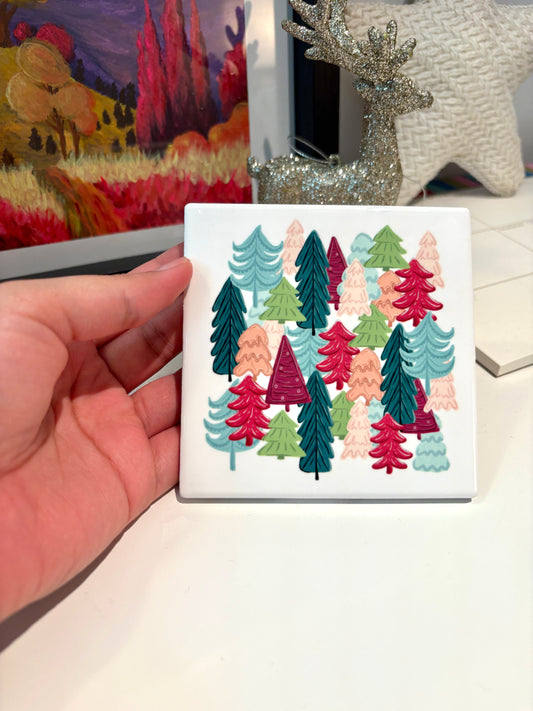Hand holding a coaster with colorful tree design in front of a painting and decorative items.